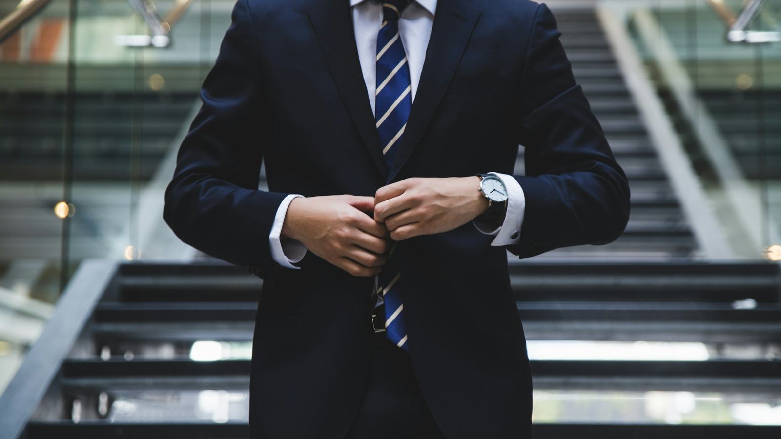 Business traveler in a suit buttoning his jacket in a corporate lobby