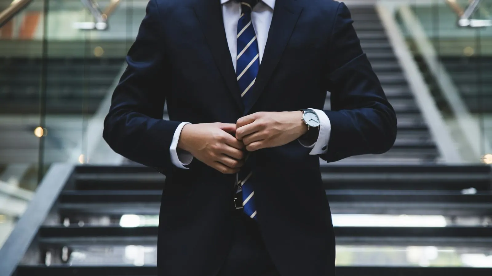 Business traveler in a suit buttoning his jacket in a corporate lobby