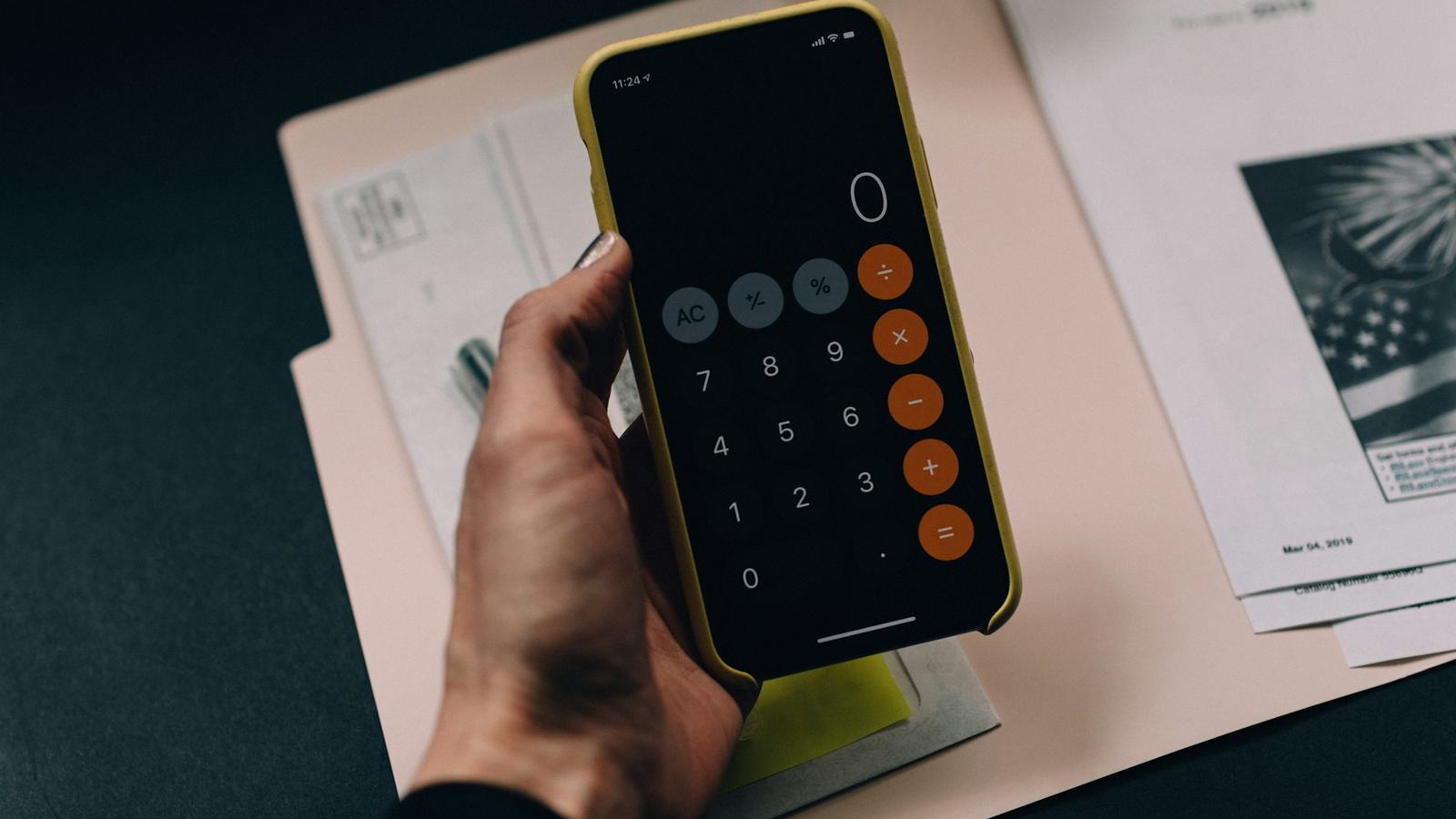 Hand holding a phone calculator over a folder of paperwork