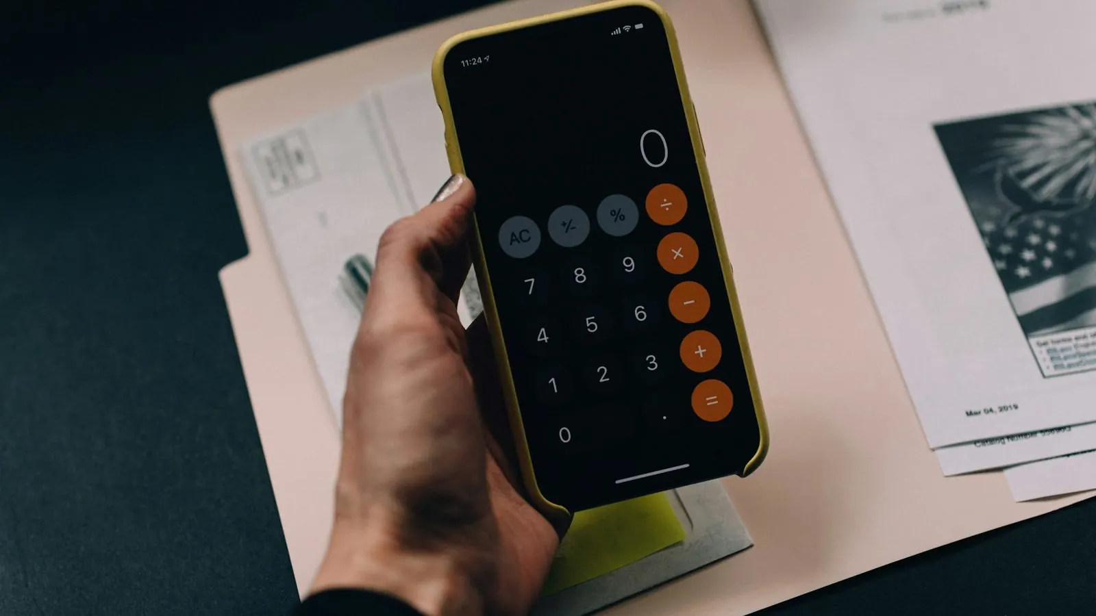 Hand holding a phone calculator over a folder of paperwork