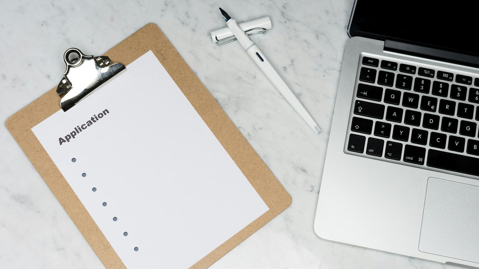 Clipboard checklist beside a laptop and pen on a marble desk