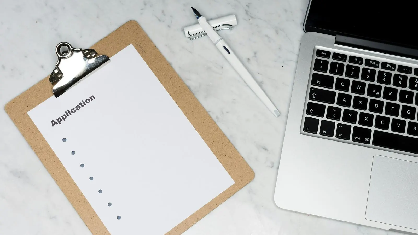 Clipboard checklist beside a laptop and pen on a marble desk
