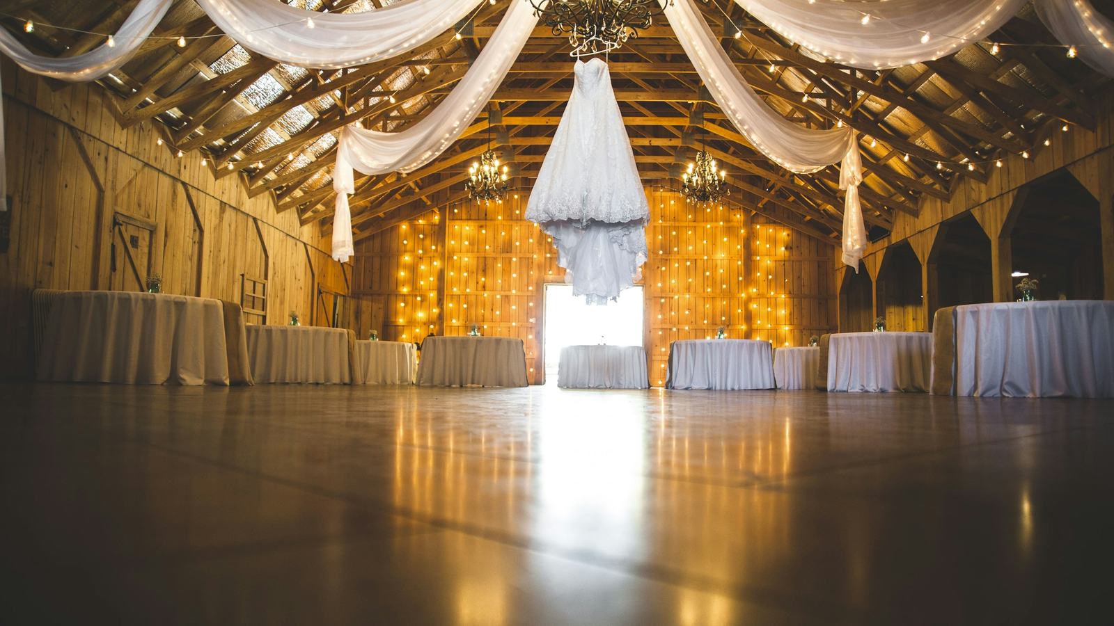 Wedding reception venue with draped fabric, chandeliers and set tables